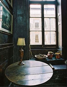 a room with a table, lamp and pictures on the wall next to an open window