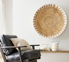 a black leather chair sitting in front of a white wall with a woven sun design on it