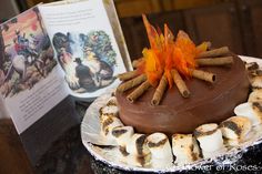 a chocolate cake with marshmallows and cinnamon sticks on top, next to an open book