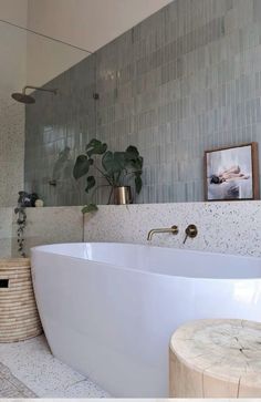 a large white bath tub sitting next to a wooden stool and potted plant in a bathroom