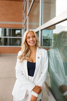 a woman in a white suit leaning against a glass wall with her hands on her hips