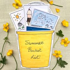 a bucket filled with pictures sitting next to yellow flowers and watercolor pencils on paper