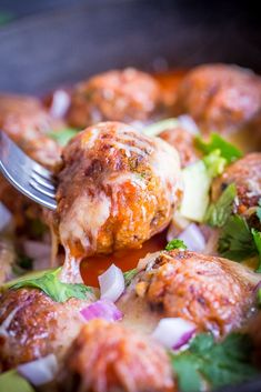 a close up of food on a fork with meatballs in sauce and vegetables around it