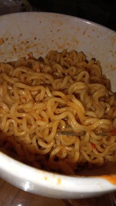 a white bowl filled with noodles on top of a wooden table