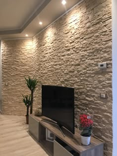 a living room with stone wall and wood flooring, tv on entertainment unit in center