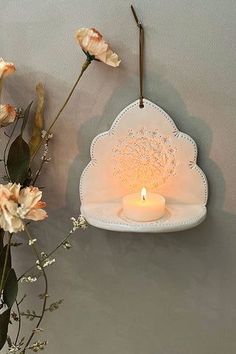 a vase with flowers and a lit candle hanging from the wall next to it on a shelf