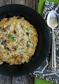 a black bowl filled with pasta and mushrooms on top of a green place mat next to a spoon