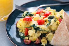 scrambled eggs with tomatoes and spinach on a blue plate next to a glass of orange juice