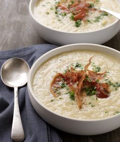 two white bowls filled with soup on top of a blue cloth next to silver spoons