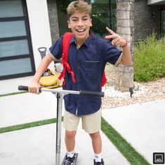 a boy with a backpack on top of a scooter pointing at the camera