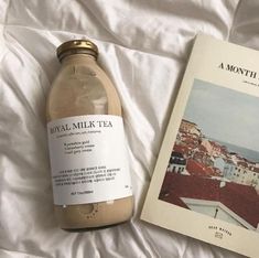 a bottle of tea sitting on top of a bed next to a book about royal milk