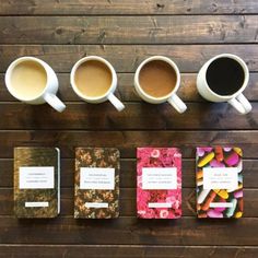 four coffee mugs sitting next to each other on top of a wooden table with notebooks