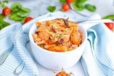 a white bowl filled with pasta on top of a blue and white towel next to tomatoes