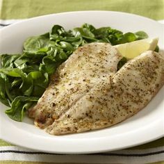 a white plate topped with chicken, spinach and lemon wedges on top of a green table cloth