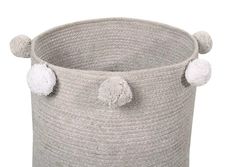 a large gray basket with pom poms on the handles and two white balls