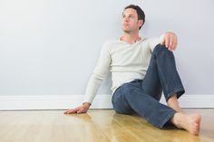 a man sitting on the floor in front of a white wall with his legs crossed