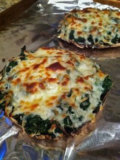 two pizzas with cheese and spinach on aluminum foil