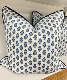 two blue and white pillows sitting on top of a wooden shelf next to a mirror