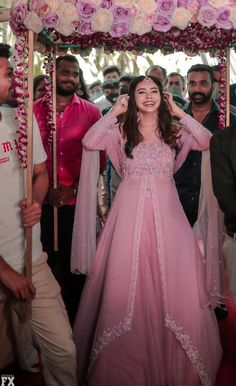 a woman in a long pink dress standing under a canopy with flowers on the side