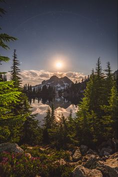 the full moon is shining over a mountain lake with trees and rocks in front of it