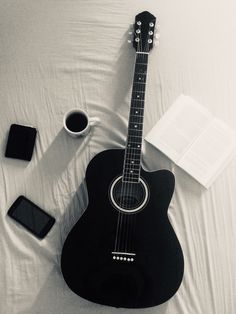 an acoustic guitar is laying on a bed next to a cup of coffee and book