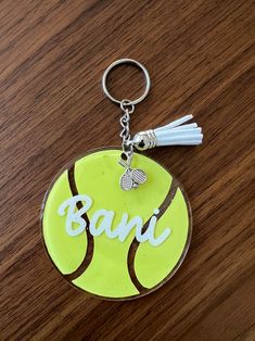 a tennis ball keychain with the word bani on it sitting on a wooden surface