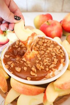 someone is dipping apples into a bowl with caramel and walnuts on the side