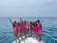 a group of women in pink bathing suits standing on the back of a sailboat