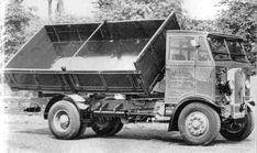 an old black and white photo of a dump truck parked in front of some trees