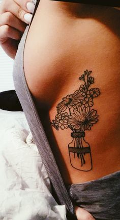 a woman with a tattoo on her stomach has flowers in a mason jar tattooed on her lower back