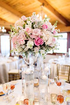 a vase filled with pink and white flowers on top of a table covered in wine glasses