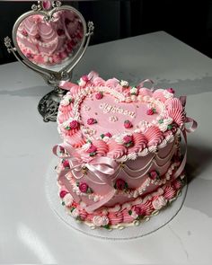 a pink heart shaped cake sitting on top of a white table next to a mirror