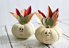 two white pumpkins decorated with leaves and faces on top of each other, sitting on a wooden surface