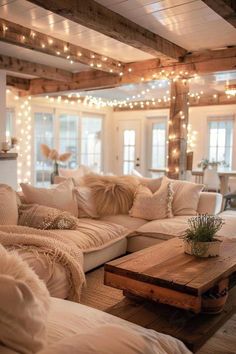 a living room filled with lots of white furniture and lights hanging from the ceiling above