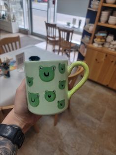 a hand holding a green coffee mug with faces on it in front of a dining room table