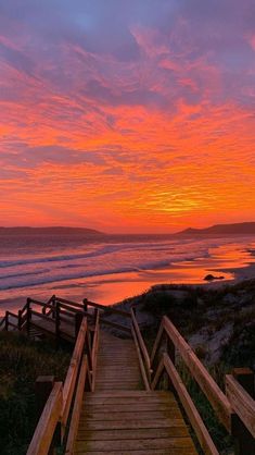 a wooden staircase leading to the beach at sunset with pink and orange clouds in the sky