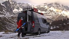 a man walking across a snow covered field next to a van with skis on top