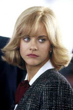 a woman with blonde hair and blue eyes wearing a jacket, red tie and earrings