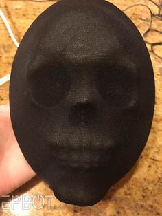 a person is holding up a black cloth skull mask that looks like a human face