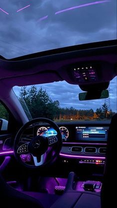 the interior of a car with purple lighting and dashboard lights in front of dark clouds