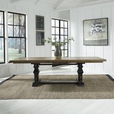 a large wooden table sitting on top of a rug in front of two black windows