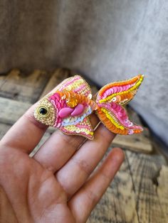 a hand holding a small colorful bird brooch