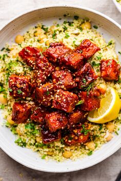 a white bowl filled with meat and rice next to a lemon wedge on top of a table