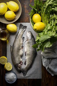 two fish sitting on top of a cutting board next to lemons and lettuce