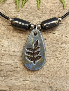 a necklace with a leaf on it and two black beads hanging from the front, sitting on top of a piece of wood