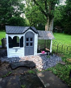 a small white chicken coop in the middle of a yard with rocks and gravel around it