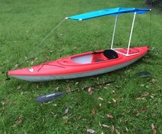 a red kayak with a blue canopy sitting in the grass next to a paddle boat