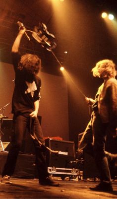 two men on stage with guitars and drums in the air, one holding up his arm