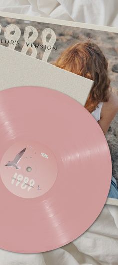 a pink record sitting on top of a bed next to a magazine and an album