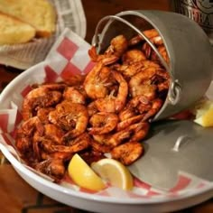 there is a bowl full of shrimp and lemon wedges next to a can of beer